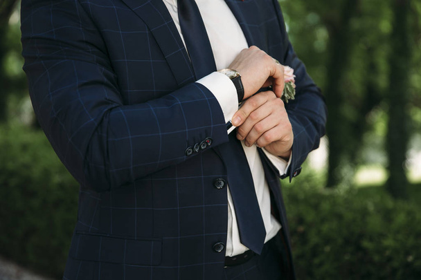 A man in a business suit, white shirt close-up of a cropped frame. The businessman puts on cufflinks, wears a gold finger ring on his finger, an expensive leather belt. - Zdjęcie, obraz