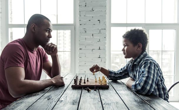 アフロ ・ アメリカ人の父とのカジュアルな服で息子がチェス家庭で一緒に時間を費やして中、側ビュー - 写真・画像