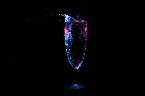 Despejando líquido em flauta de champanhe em luz azul e vermelha em um fundo preto
 - Foto, Imagem