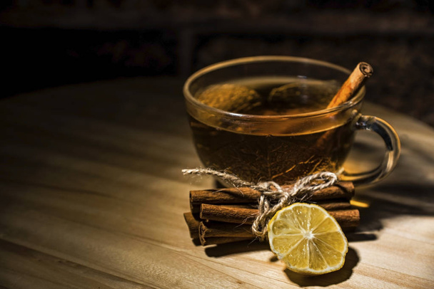 A cup of tea with a cinnamon sticks and a lemon slice on a wooden table, close up - Фото, изображение