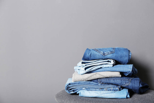 Stack of different jeans on stool against gray background. Space for text - Фото, зображення
