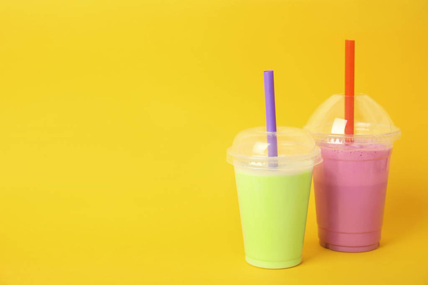 Plastikbecher mit leckeren Milchshakes und Platz für Text auf farbigem Hintergrund - Foto, Bild