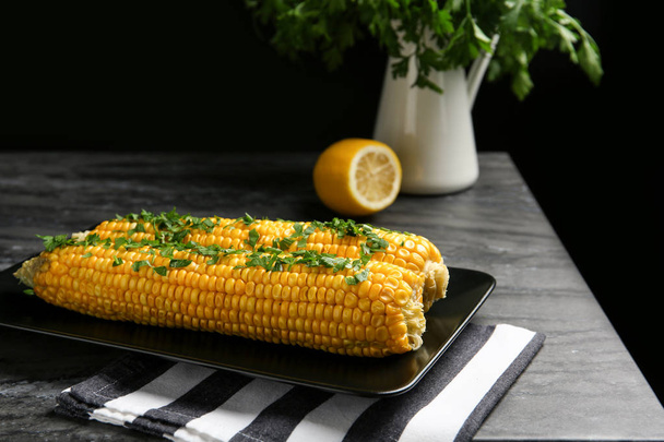 Delicious boiled corn cobs with parsley on gray table against black background - Foto, immagini