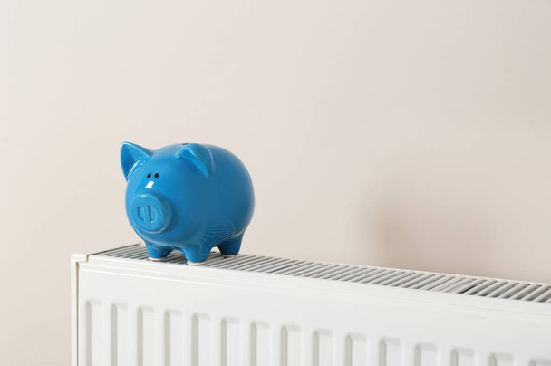 Piggy bank on heating radiator against light background - Foto, Imagen