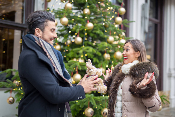 Счастливый молодой человек дарит рождественский подарок своей девушке, пока она улыбается
 - Фото, изображение