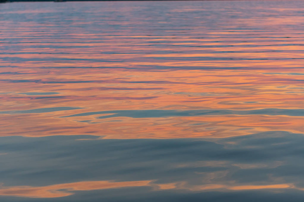 Rózsaszín naplemente fény tükrözi a nyugodt víz hullámai - Fotó, kép