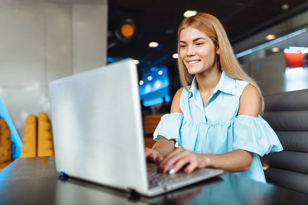 Piękna młoda pozytywne dziewczyna pracuje na laptopie, zakupy przez Internet, siedząc w kawiarni przy stole - Zdjęcie, obraz
