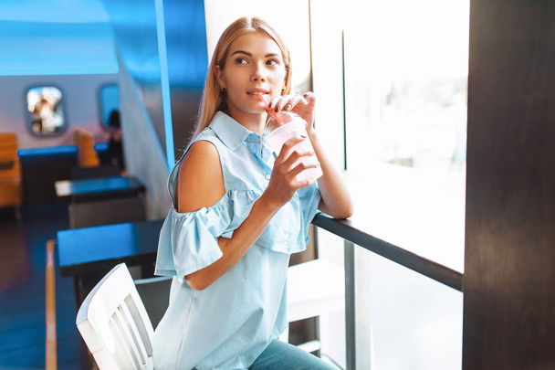 Beautiful young cheerful girl, drinking a cocktail, sitting in a cafe and waiting for someone - Foto, imagen