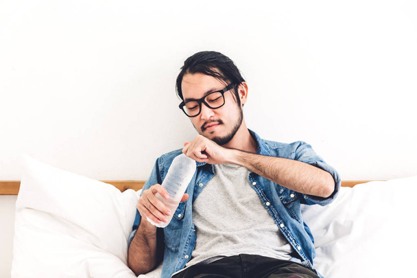 Jeune homme sain buvant de l'eau d'une bouteille tout en se relaxant et se sentant frais à la maison
 - Photo, image