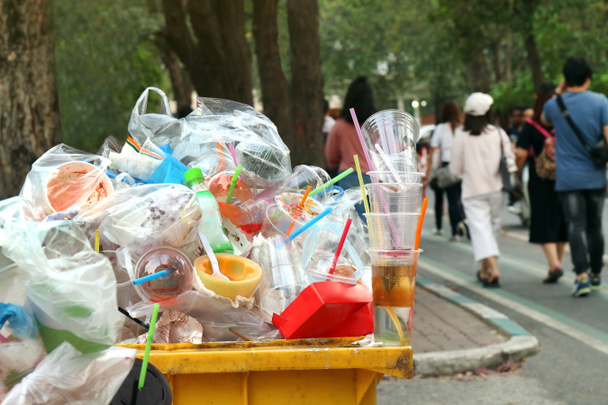 Сміттєві відходи, повні сміттєвих відходів жовтого кольору і фону, люди ходять по тротуарному саду, сміттєвих відходів, сміттєвого пластику, сміття, відходів, пластикових відходів
 - Фото, зображення