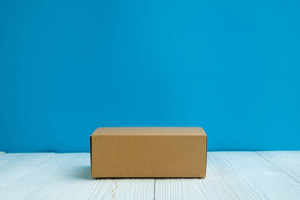 Empty Package brown cardboard box or tray on bright white wooden table with blue wall background. copy space for add text or advertising word. - Фото, зображення