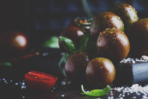 Brown cherry tomatoes with sea salt and green basil on dark table, autumn harvest, selective focus  - Foto, afbeelding