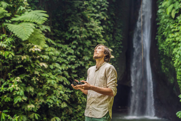 Man controlling drone with tropical plants and waterfall at background  - 写真・画像