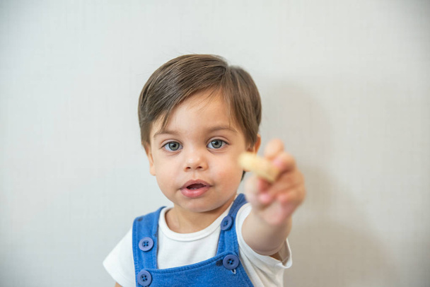 Bebê bonito criança - com romper azul no fundo branco - Comer wafer
 - Foto, Imagem