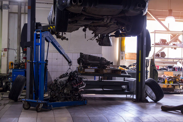 車輪の両側に横になっている青いクレーンと車両修理工場でリフティング テーブルにギヤボックス懸戸エンジン修理のため、その下にリフトで発生したスポーツ車 - 写真・画像