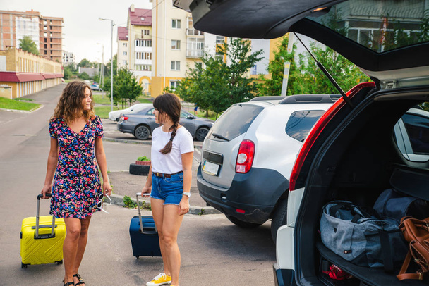 две женщины упаковывают багаж в багажник машины. Дорожная поездка
 - Фото, изображение