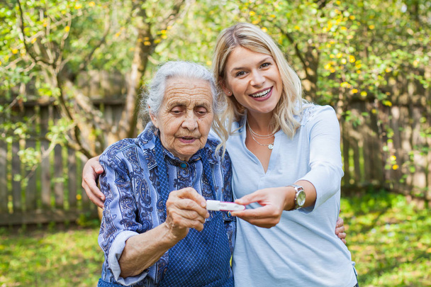 Happy woman expecting a baby, holding pregnancy test, spending time with future great-grandmother - Photo, Image