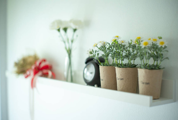 花瓶の背景がぼやけている陶器の花で飾られた白い木製の棚にヴィンテージ目覚まし時計を置きます - 写真・画像