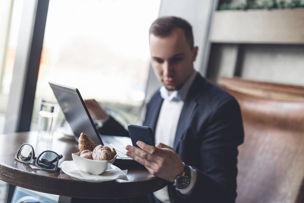Young, modern and positive business man sitting in cafe and doing his job on notebook, cellphone and tablet. - Foto, imagen