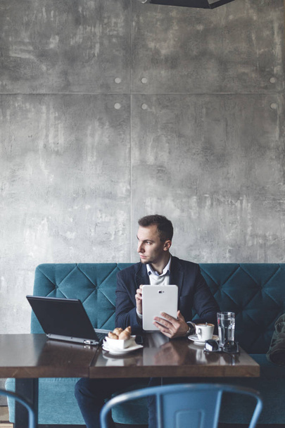 Young, modern and positive business man sitting in cafe and doing his job on notebook, cellphone and tablet. - Photo, Image