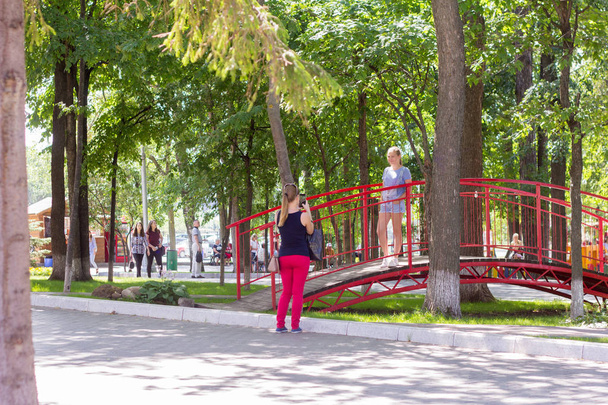 Iżewsk, Rosja, 31 lipca, 2018.People gulyayut w lato Park, dziewczyna robi zdjęcia z przyjaciółką na smartfonie - Zdjęcie, obraz