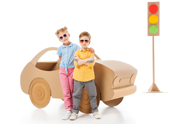 stylish kids in sunglasses posing near cardboard car and traffic lights, on white - Photo, Image