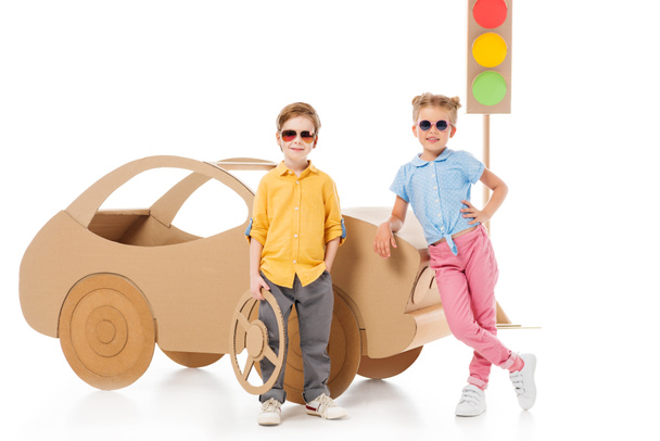 κομψό παιδιά σε γυαλιά ηλίου θέτοντας κοντά στο αυτοκίνητο από χαρτόνι και φώτα κυκλοφορίας, σε λευκό  - Φωτογραφία, εικόνα