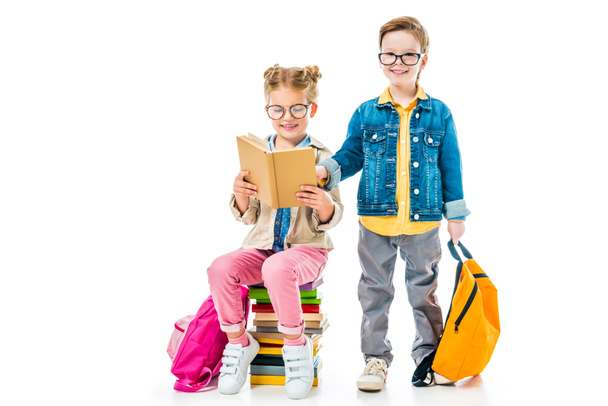 schoolchildren in eyeglasses studying and sitting on books with backpacks, isolated on white  - Fotografie, Obrázek