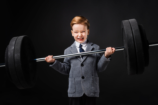 strong little boy in suit lifting barbell isolated on grey - Φωτογραφία, εικόνα