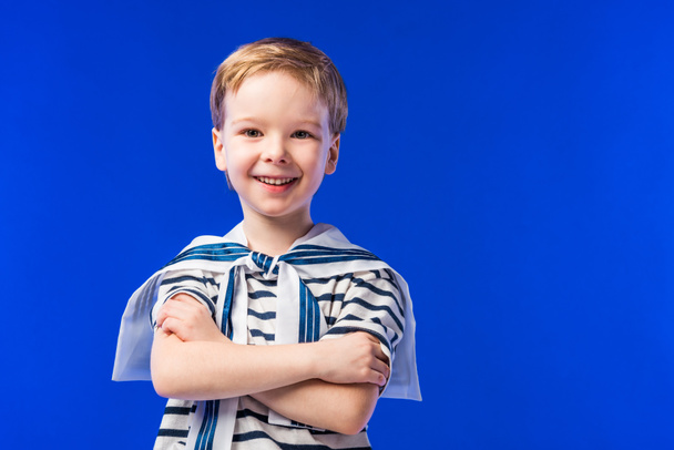 uśmiechnięty chłopiec pozowanie w t-shirt w paski z skrzyżowanymi rękami, na niebieskim tle - Zdjęcie, obraz
