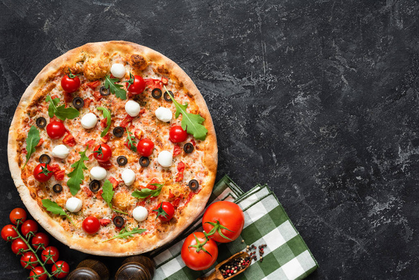 Tasty pizza on black concrete background, top view and copy space for text. Italian pizza with tomato, mozzarella cheese, black olives and arugula - Foto, afbeelding