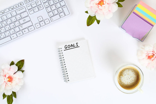 Write a goal for the new year 2010 in a white notebook on a white desktop next to a coffee mug and a keyboard. Top view, flat layout - 写真・画像