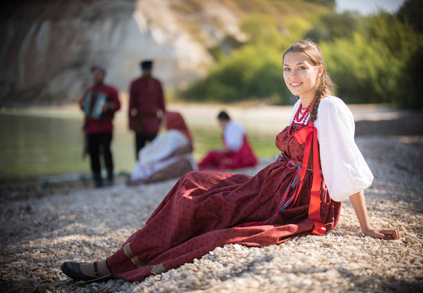 Piękna dziewczyna w czerwonym stroju narodowego rosyjski stanowią dla aparatu na tle niesamowity krajobraz - Zdjęcie, obraz