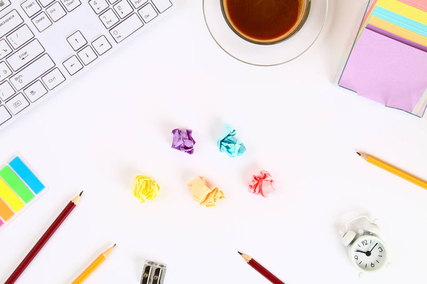 Hojas de papel multicolores arrugadas en un escritorio blanco junto a una taza de café y un teclado. Vista superior, plano. Copiar el espacio
 - Foto, imagen