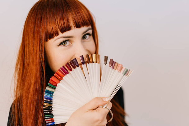 red-haired woman holds samples of a gel-varnish in her hand in the form of a semicircle on a white background. Close-up - Photo, image