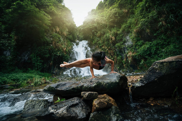Young woman practicing yoga near waterfall in forest - Foto, Imagen