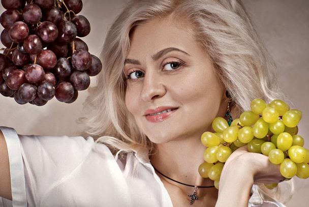 young, pretty blonde with grapes on a photo studio. natural makeup. - Foto, afbeelding