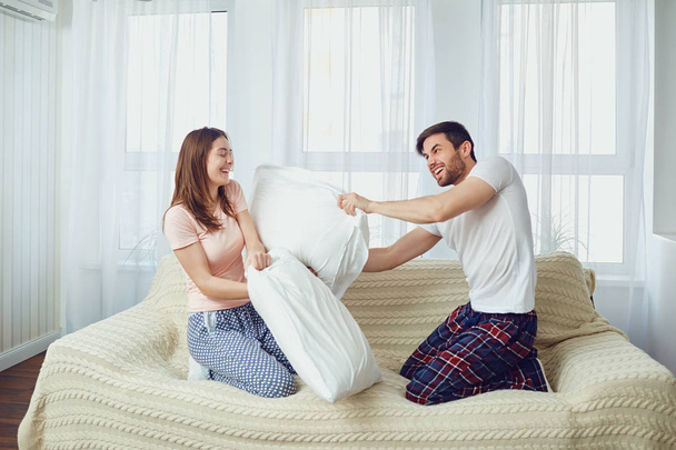 Couple in bed having fun fighting pillows in the room - Foto, afbeelding
