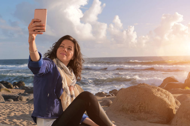 Beautiful caucasian woman taking selfie on smartphone on beach - Valokuva, kuva