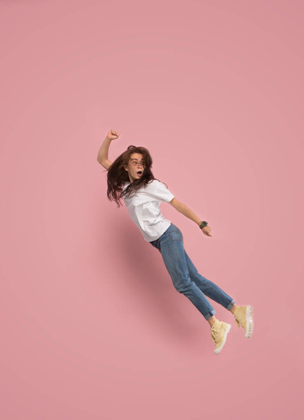Freedom in moving. Pretty young woman jumping against pink background - Zdjęcie, obraz