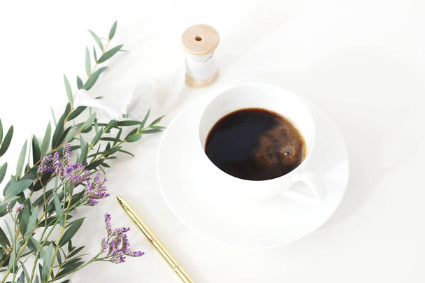 Wedding styled stock photo. Breakfast still life with eucalyptus leaves, limonium, babys breath Gypsophila flowers, golden pen and cup of coffee. Floral composition. Selective focus. - Foto, afbeelding