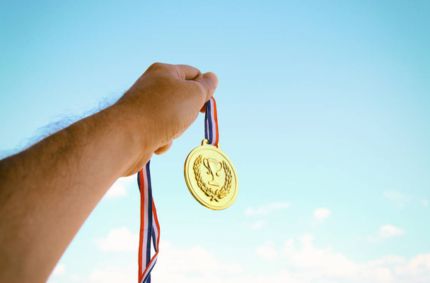 main levée, tenant la médaille d'or contre le ciel. concept de récompense et de victoire - Photo, image