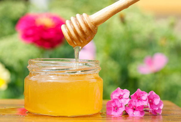Tarro de miel, palo y flor rosa en mesa de madera
 - Foto, Imagen