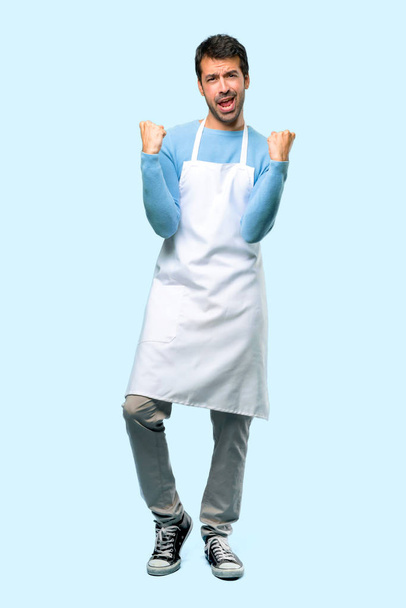 Full body of Man wearing an apron celebrating a victory and happy for having won a prize on blue background - Photo, Image