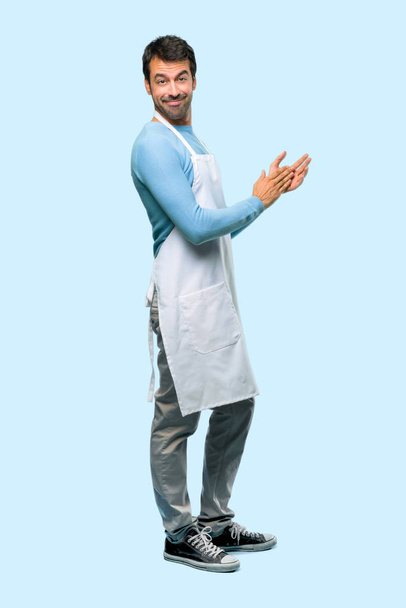 Volledige lichaam van Man, het dragen van een schort applaudisseren na de presentatie in een conferentie op blauwe achtergrond - Foto, afbeelding