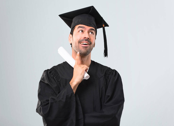 Man on his graduation day University standing and thinking an idea on grey background - Φωτογραφία, εικόνα