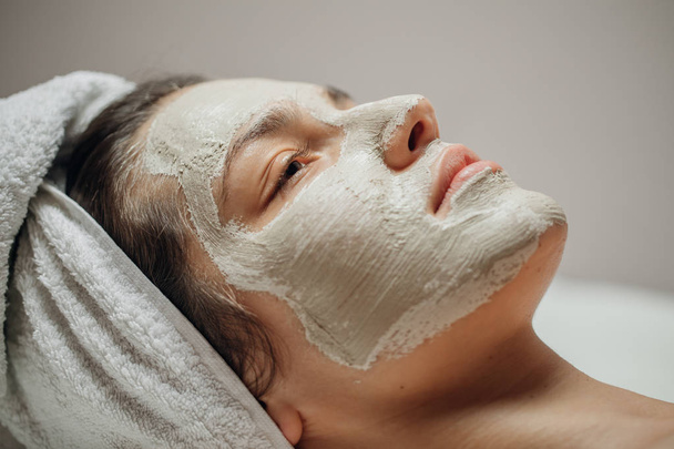 Beautiful young Caucasian woman with a natural facial mask on her face lying on the massage table. - Photo, Image