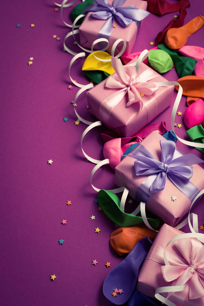 Sfondo festivo di materiale viola palloncini colorati stelle filanti coriandoli quattro scatole regalo. Vista dall'alto lastra piatta copia spazio tonificazione
 - Foto, immagini