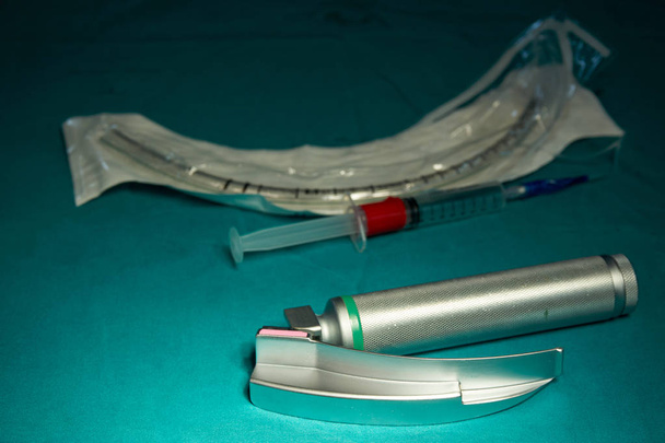 Laringoscopio, tubo endotraqueal, jeringa sobre mesa verde en quirófano
                                - Foto, Imagen
