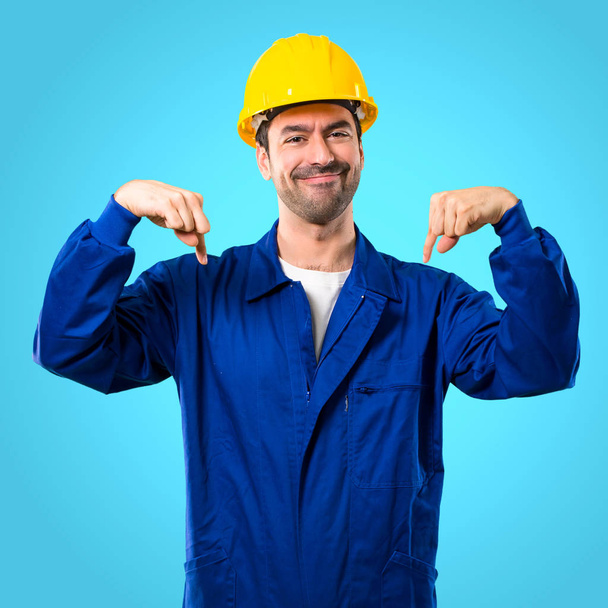 Jeune ouvrier avec casque pointant vers le bas avec les doigts sur fond bleu
 - Photo, image